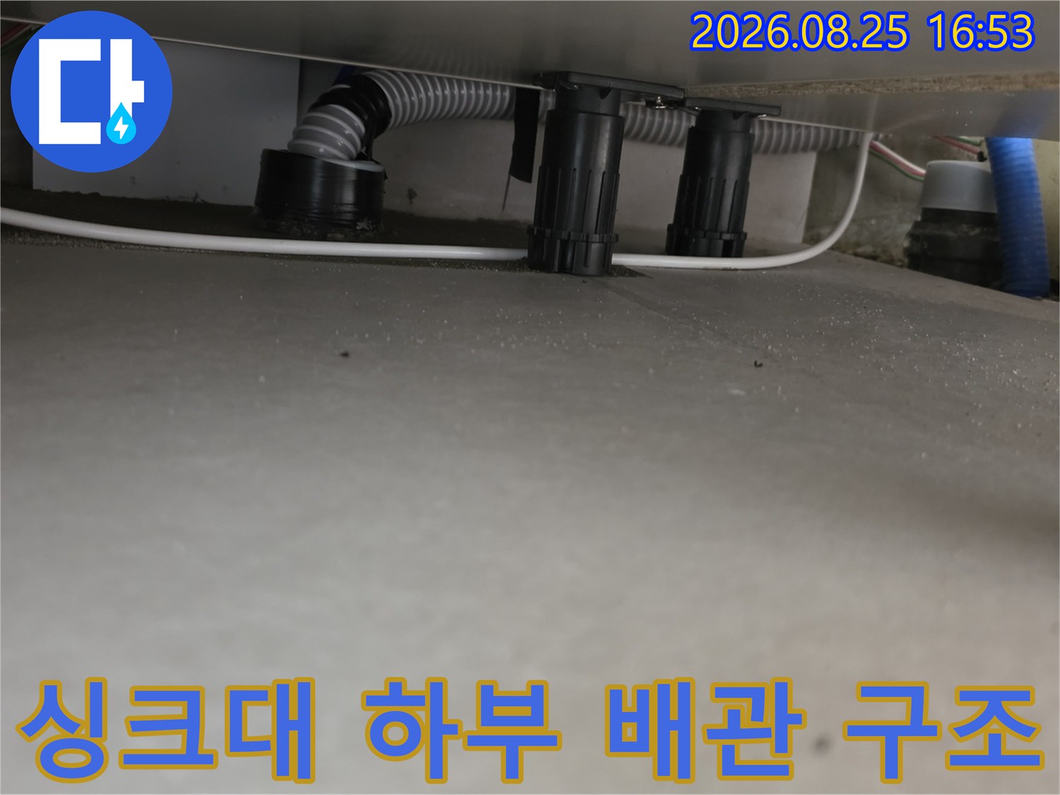 싱크대 밑에 설치된 회색 주름관과 검은색 연결 부위의 모습입니다.