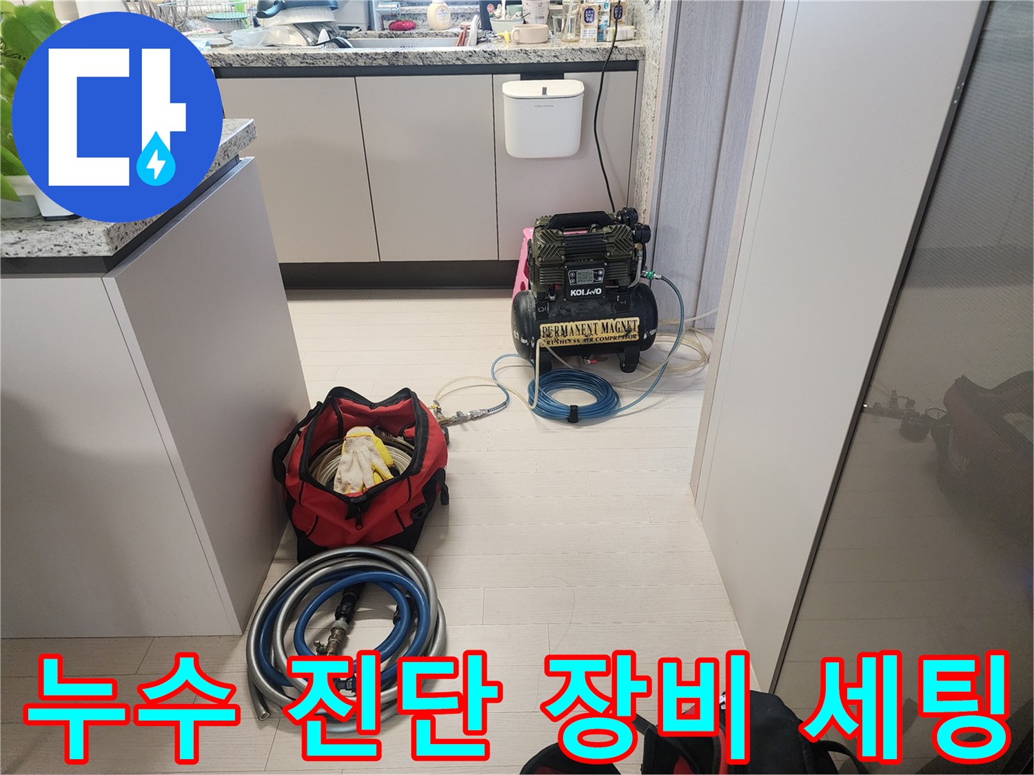 싱크대 하단 공간에 놓인 검정색 공압 장비와 파란색 호스 연결부