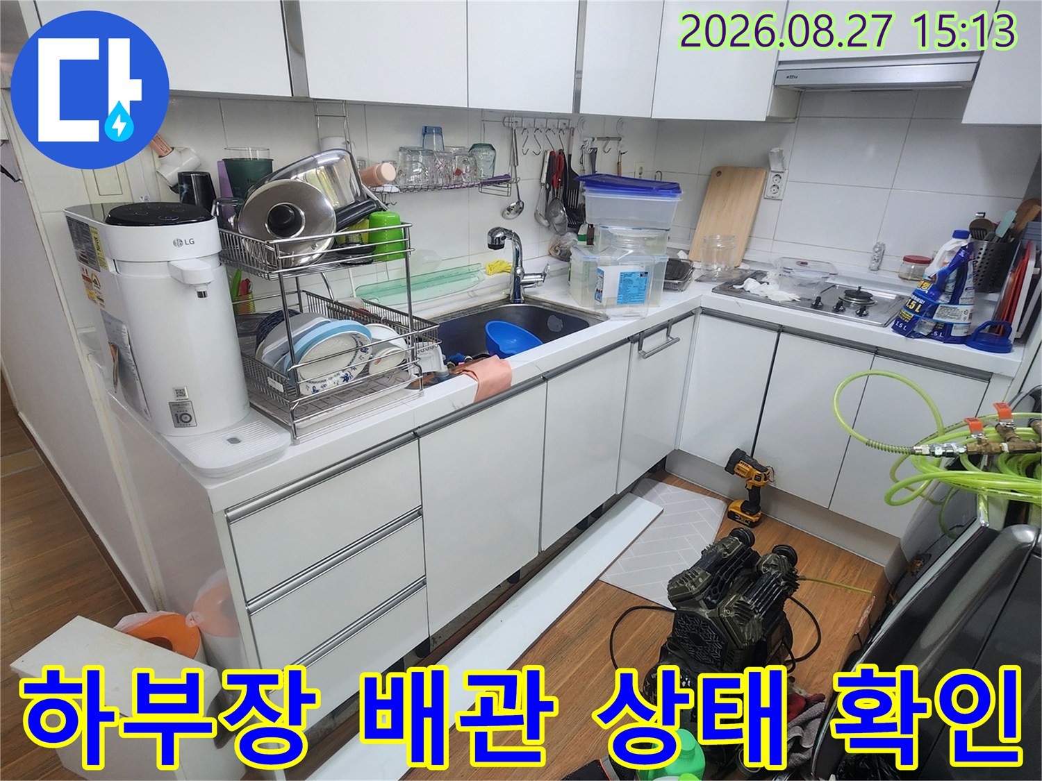 싱크대 하부 공간에 복잡하게 연결된 보일러 분기점과 배관들을 점검하는 사진입니다.
