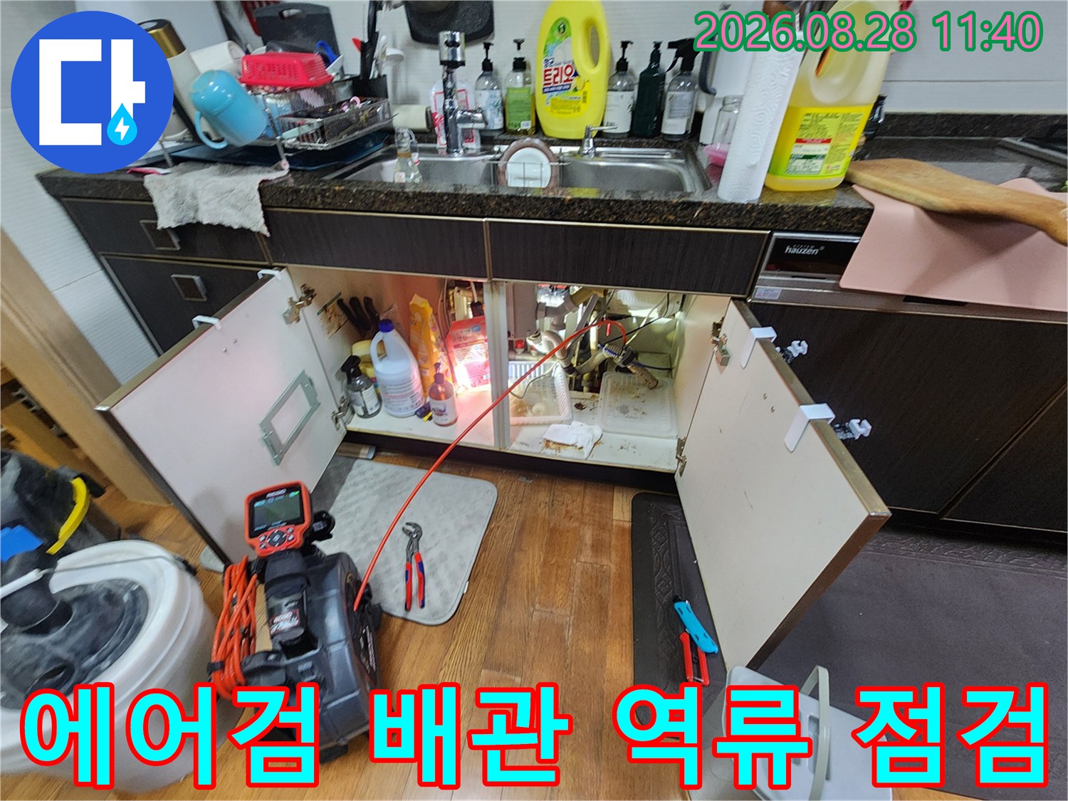 에어컨 응축수 배관의 막힘과 역류 지점을 찾기 위해 하부장을 열고 검사하는 장면입니다.