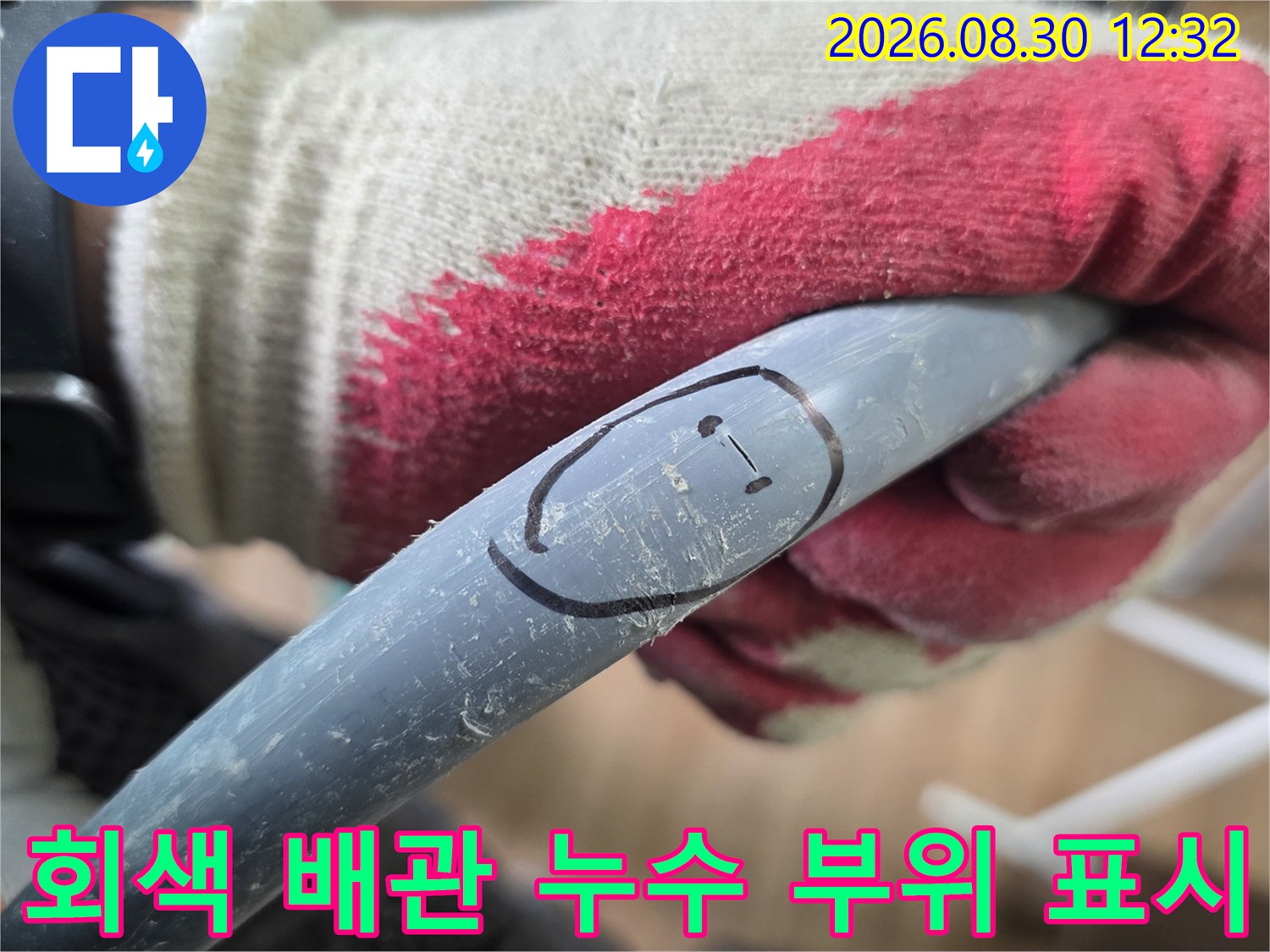 손으로 잡고 있는 회색 배관-검은색 펜으로 누수 지점을 표시한 모습