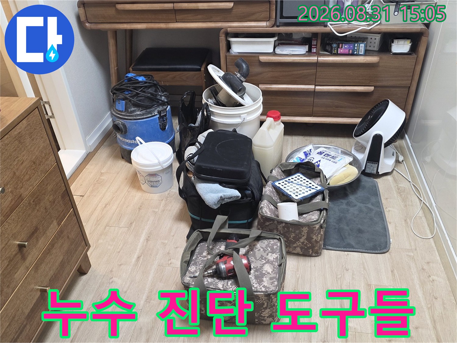 배관 누수 지점을 찾기 위해 거실 바닥에 준비된 점검용 장비와 용기