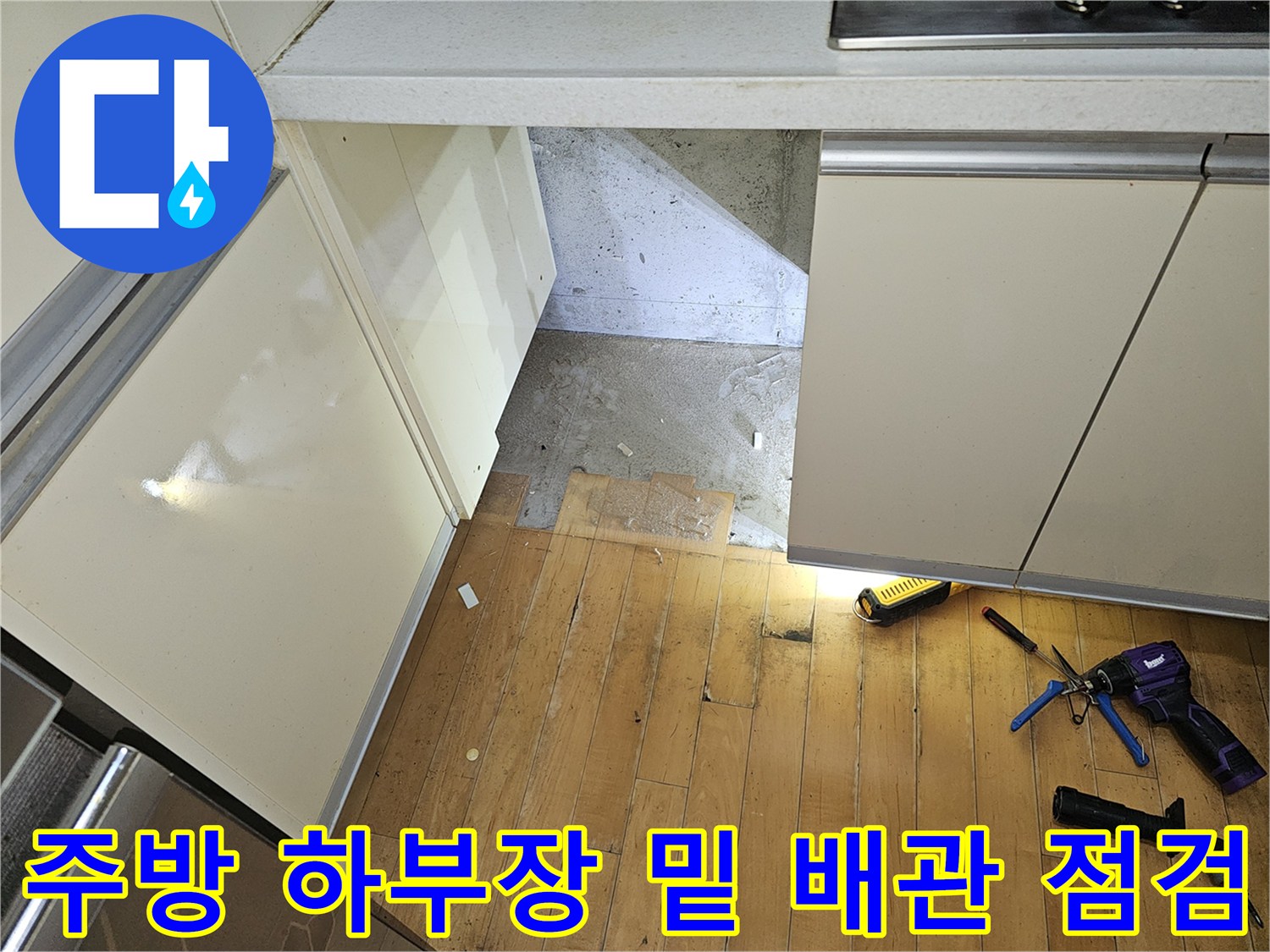 싱크대 하부장 아래 노출된 배관 통로와 작업용 도구들