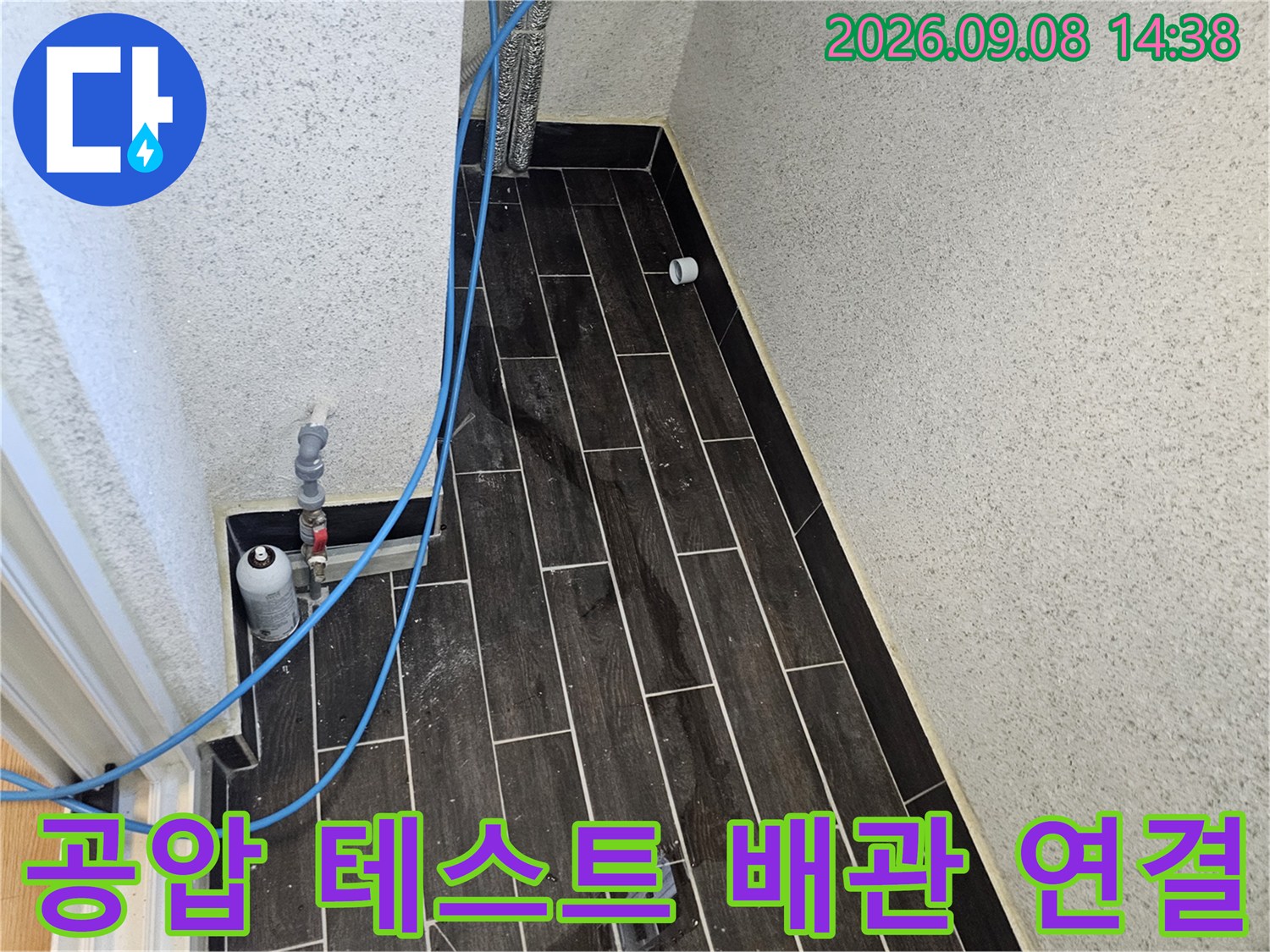 어두운 타일 벽체-파란색 호스와 압력을 조절하는 밸브 장치 상세 모습
