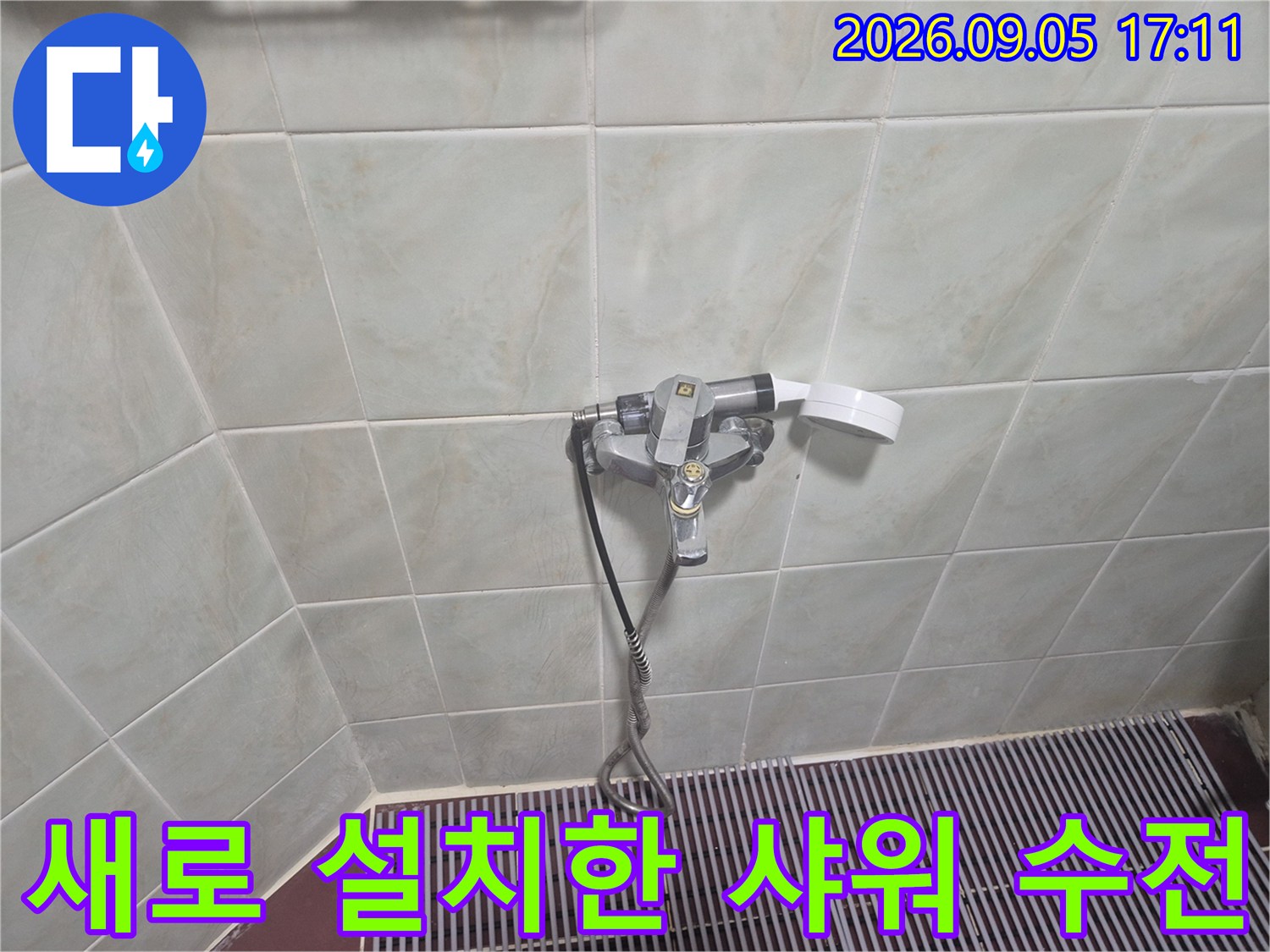 타일 벽면에 설치된 은색 샤워 수전과 배수구 주변 모습입니다.