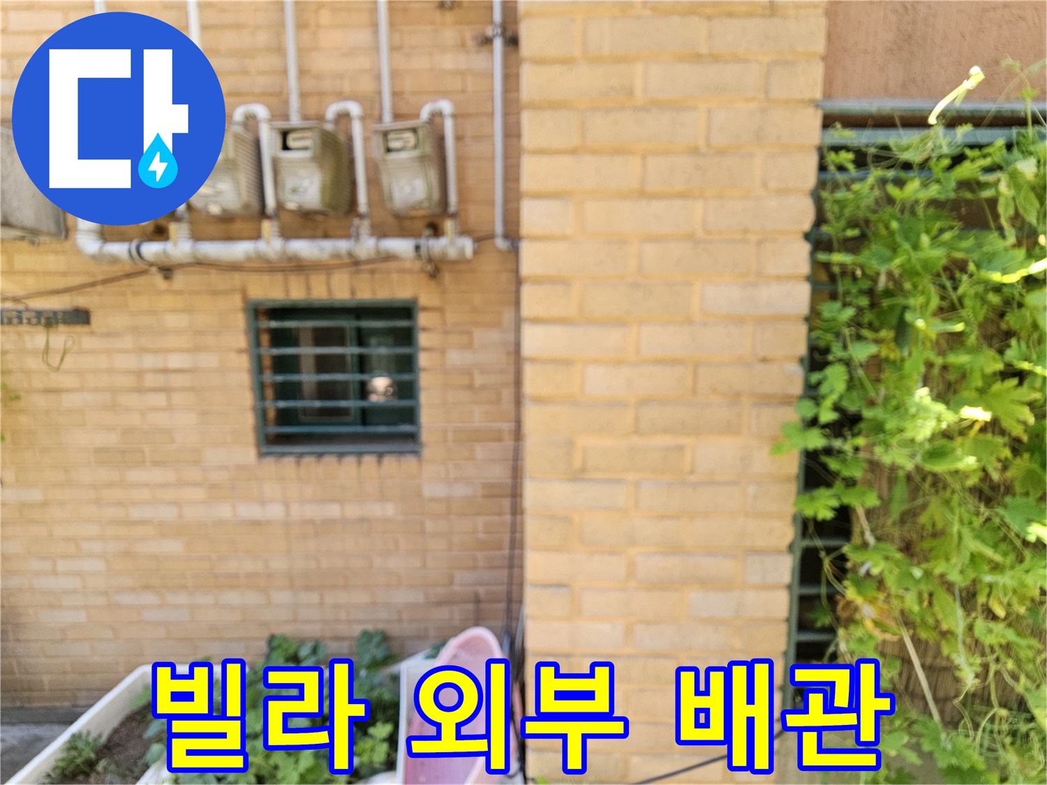 벽돌 외벽에 설치된 수도 계량기와 흰색 연결 배관의 모습