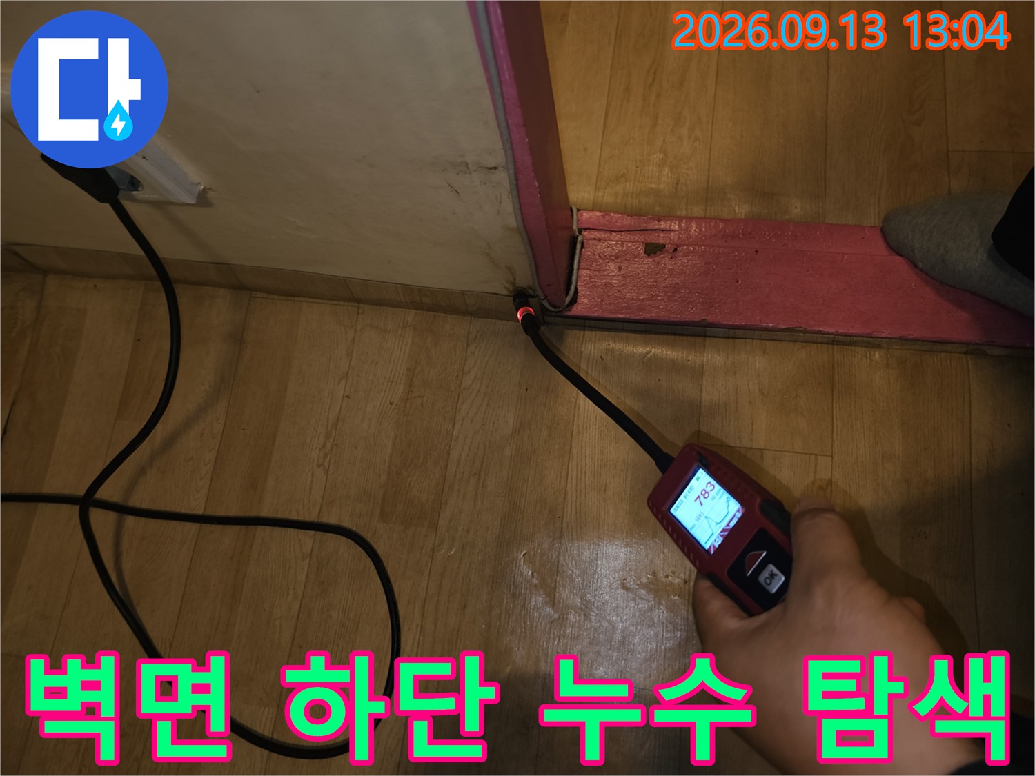 벽면과 바닥의-경계 지점에 탐지기를 위치시켜 점검하는 장면입니다.
