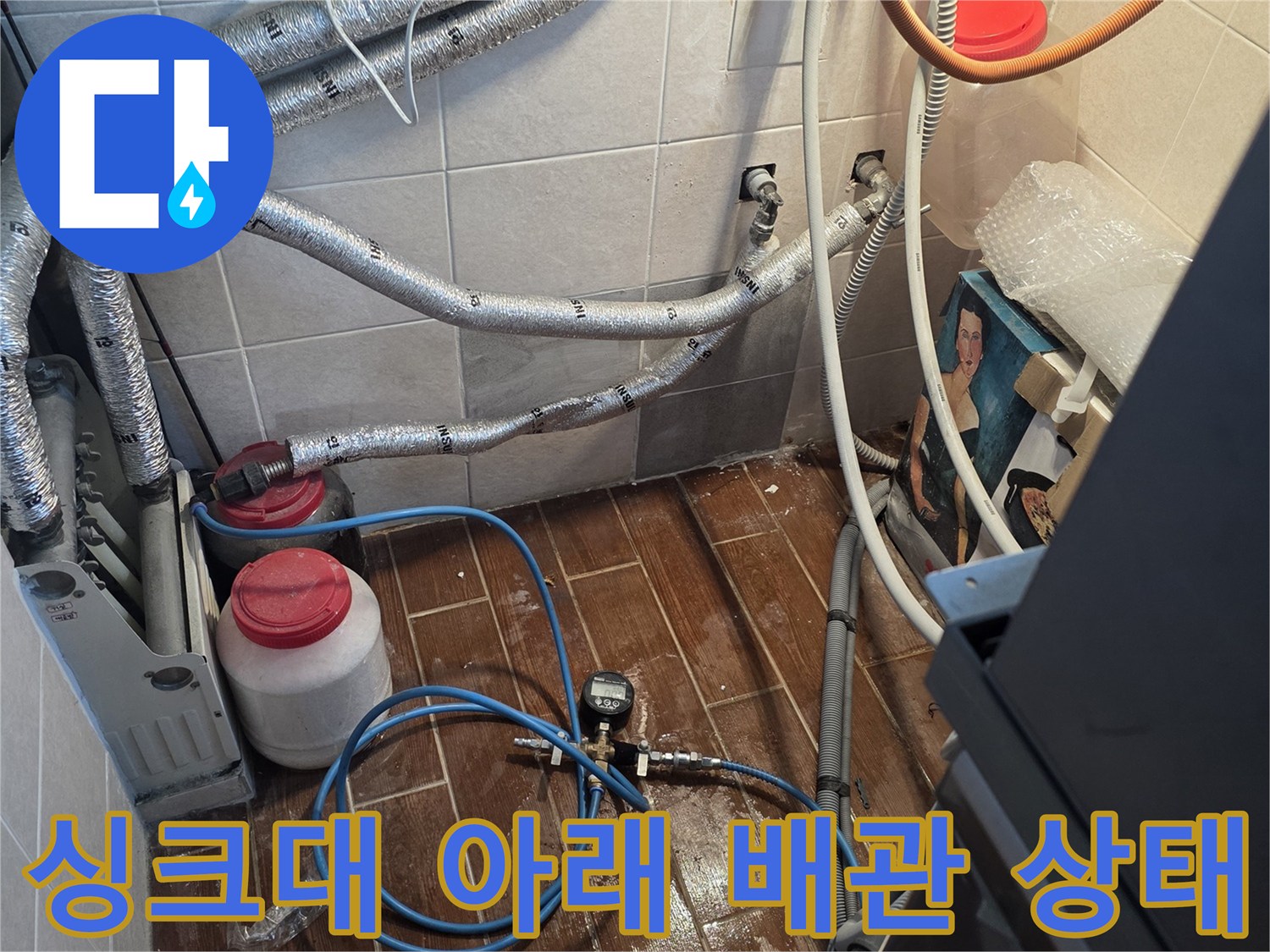 주방 싱크대 하부장 아래 노출된 은박 보온재 배관과 연결 부위 모습